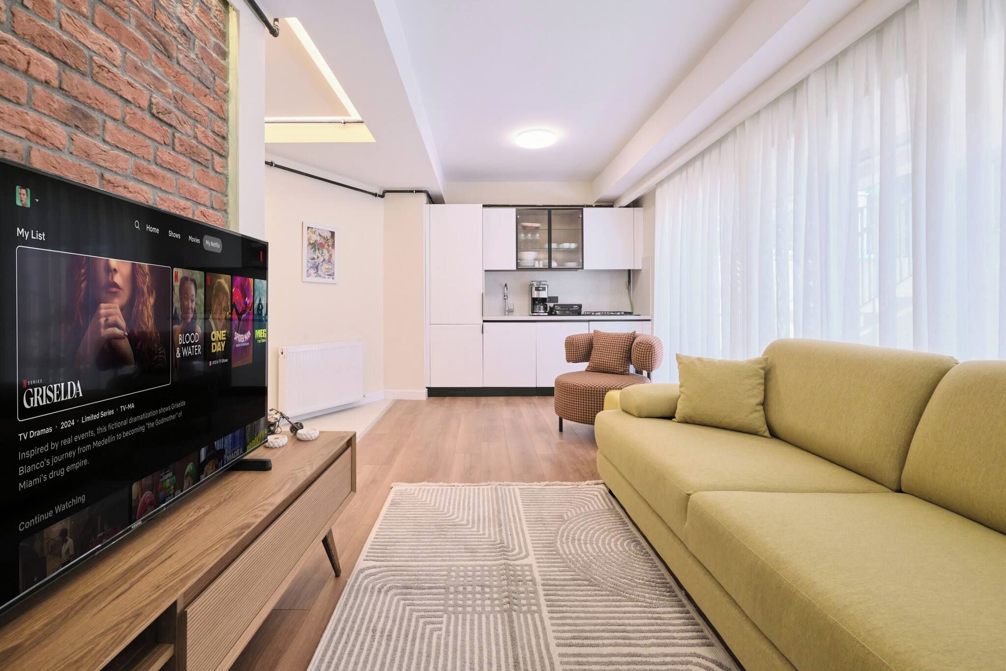 Ein modernes Wohnzimmer mit Flachbildfernseher, einer Couch, einer Küchenzeile und einem Esstisch.