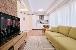 A modern living room with a flat-screen TV, a sofa, a kitchen area, and a dining table. - Arcturus, 2BR, Best Loc (Kadıköy)