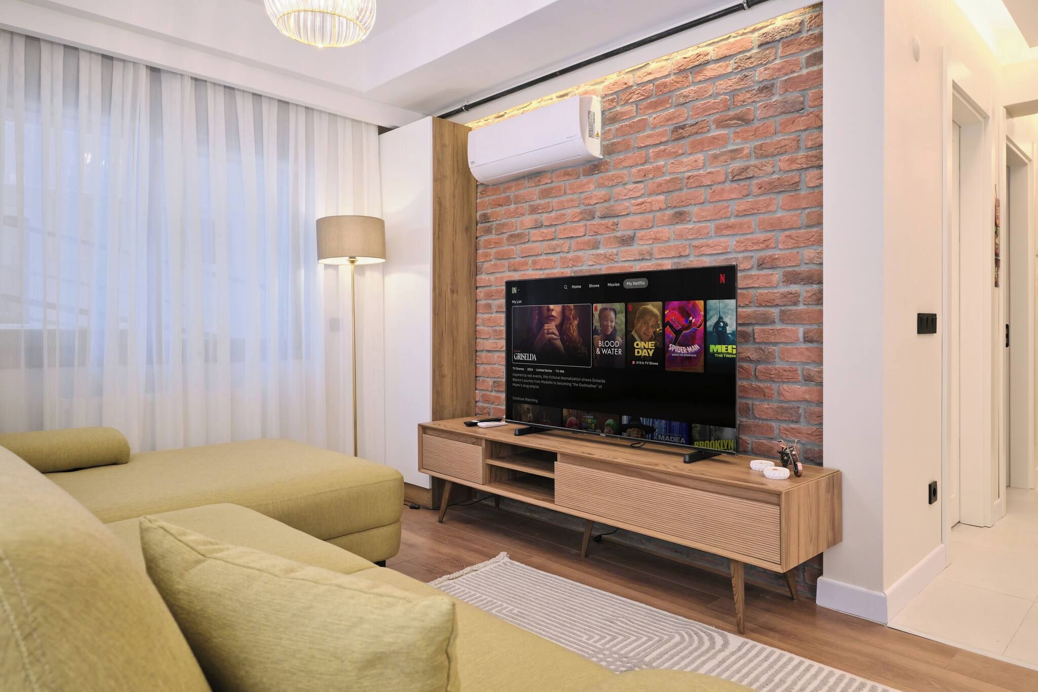 Un salon moderne avec un téléviseur à écran plat fixé à un mur en briques, un canapé et une lampe sur pied.