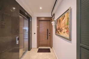 A hallway with a wooden door, a digital elevator control panel, and a framed painting on the wall. - Arcturus, 2BR, Best Loc (Kadıköy)