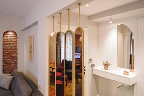 Ein modernes Interieur mit einer Ziegelwand, einer Couch, einem weißen Konsolentisch mit Spiegel und einer Schiebetür mit goldener Rahmung.