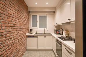 A compact kitchen with a brick wall, white cabinets, a built-in oven, and a coffee machine. - Renovated, Stylish, 3BR Kadıköy (Kadıköy)