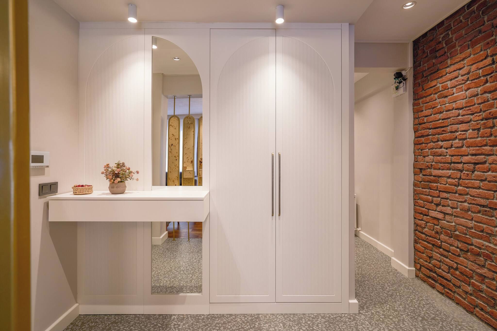 A hallway with a white wardrobe, a mirror, and a small table with a vase.
