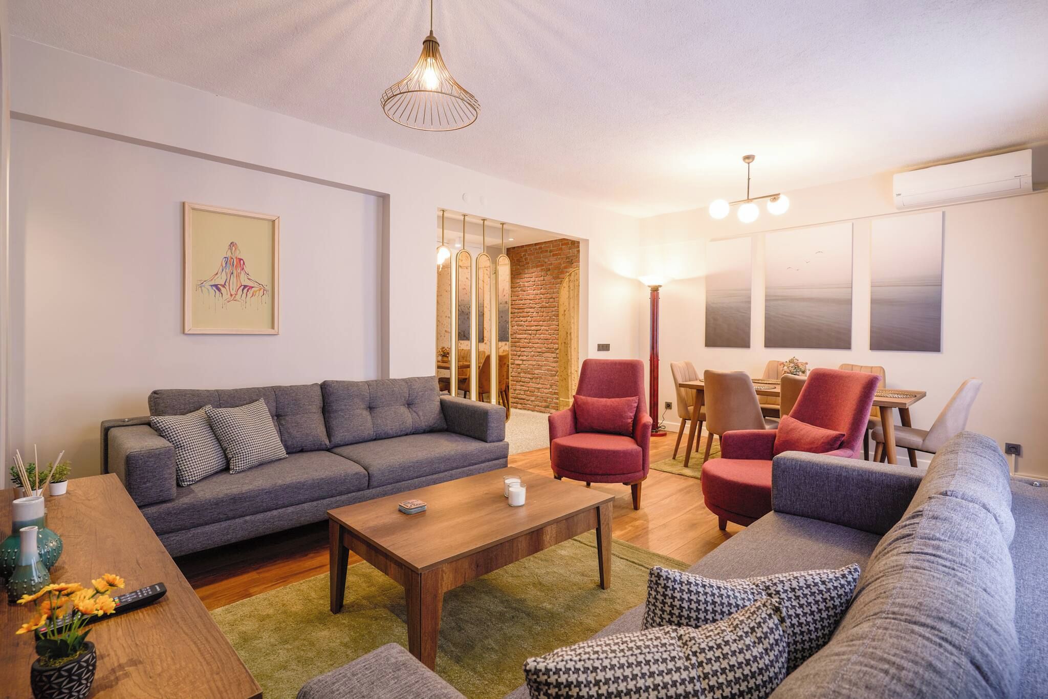 A modern living room with a grey sofa, red armchairs, a wooden coffee table, and a dining area with a table and chairs.
