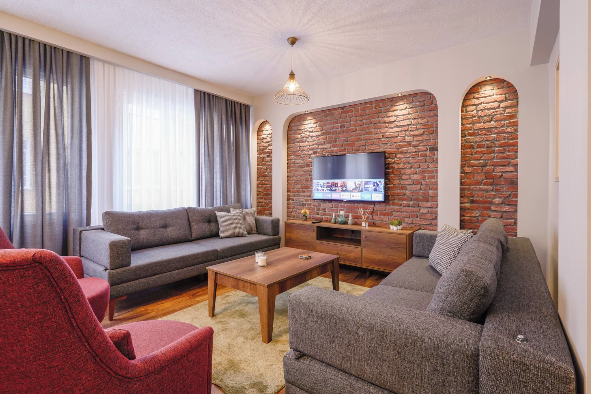 A living room with a sofa, armchairs, a coffee table, and a TV mounted on a brick wall.