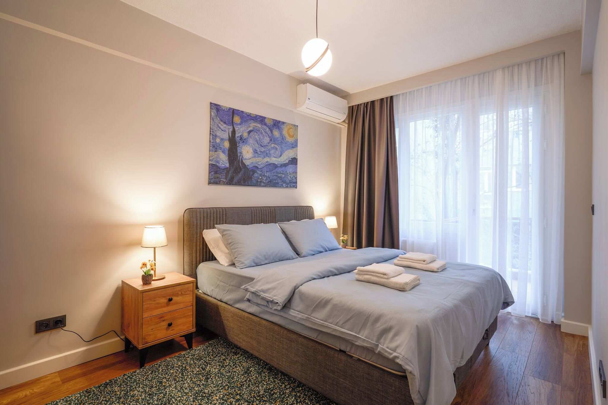 A bedroom with a bed, bedside table, lamp, and a painting on the wall.