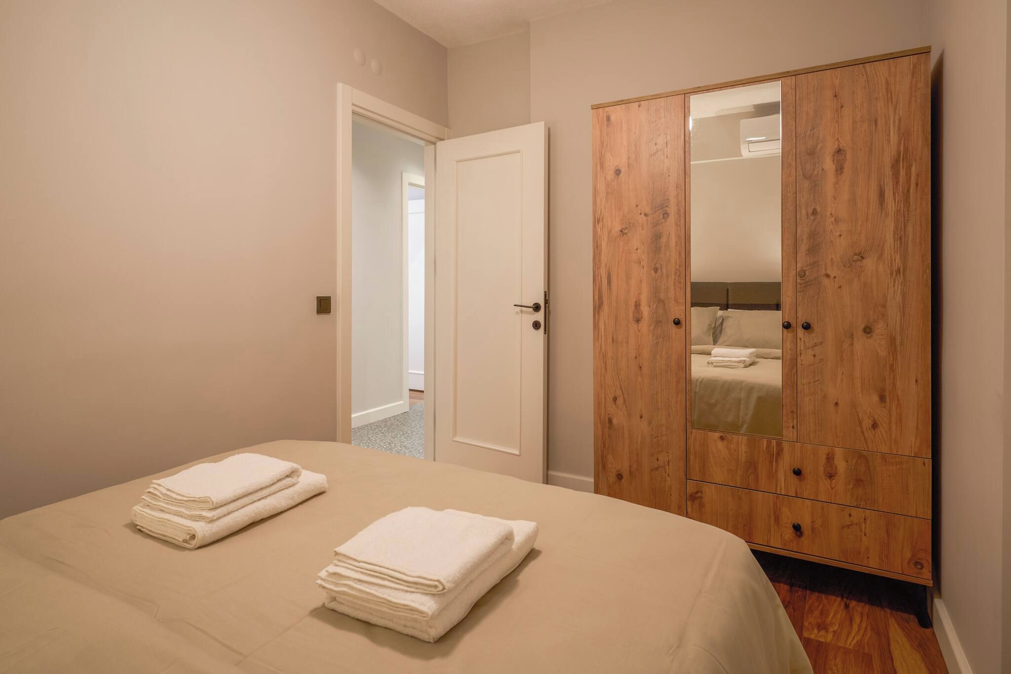 Une chambre à coucher avec un lit, deux serviettes pliées, une armoire en bois et une porte donnant sur une autre pièce.