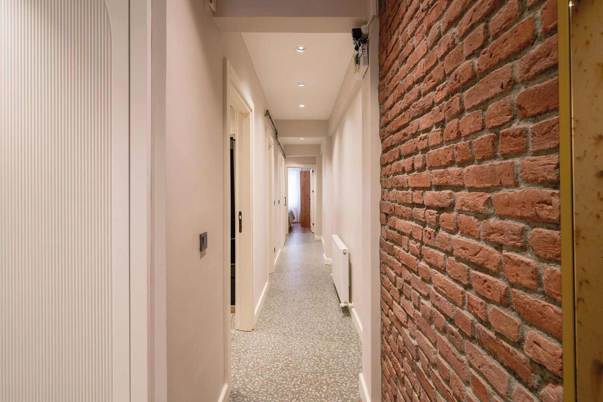 A hallway with a brick wall on one side and a white door on the other, leading to a room with a bed.