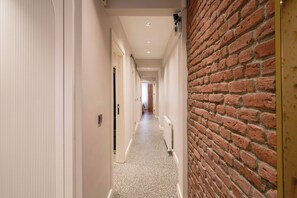 A hallway with a brick wall on one side and a white door on the other, leading to a room with a bed. - Renovated, Stylish, 3BR Kadıköy (Kadıköy)