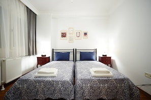 A double bed with a patterned bedspread, two bedside tables, a radiator, and a window with curtains. - Elite, Tastefully Furnished, 3BR (Kadıköy)