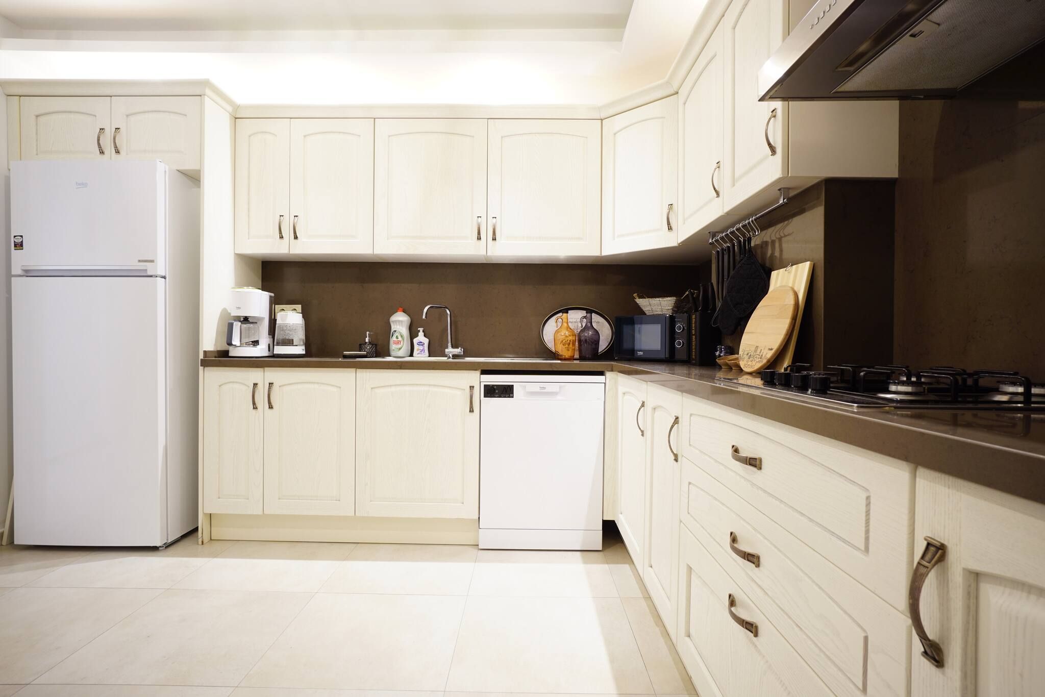 A kitchen with white cabinets, a white refrigerator, a dishwasher, a coffee maker, a microwave, and a stove.