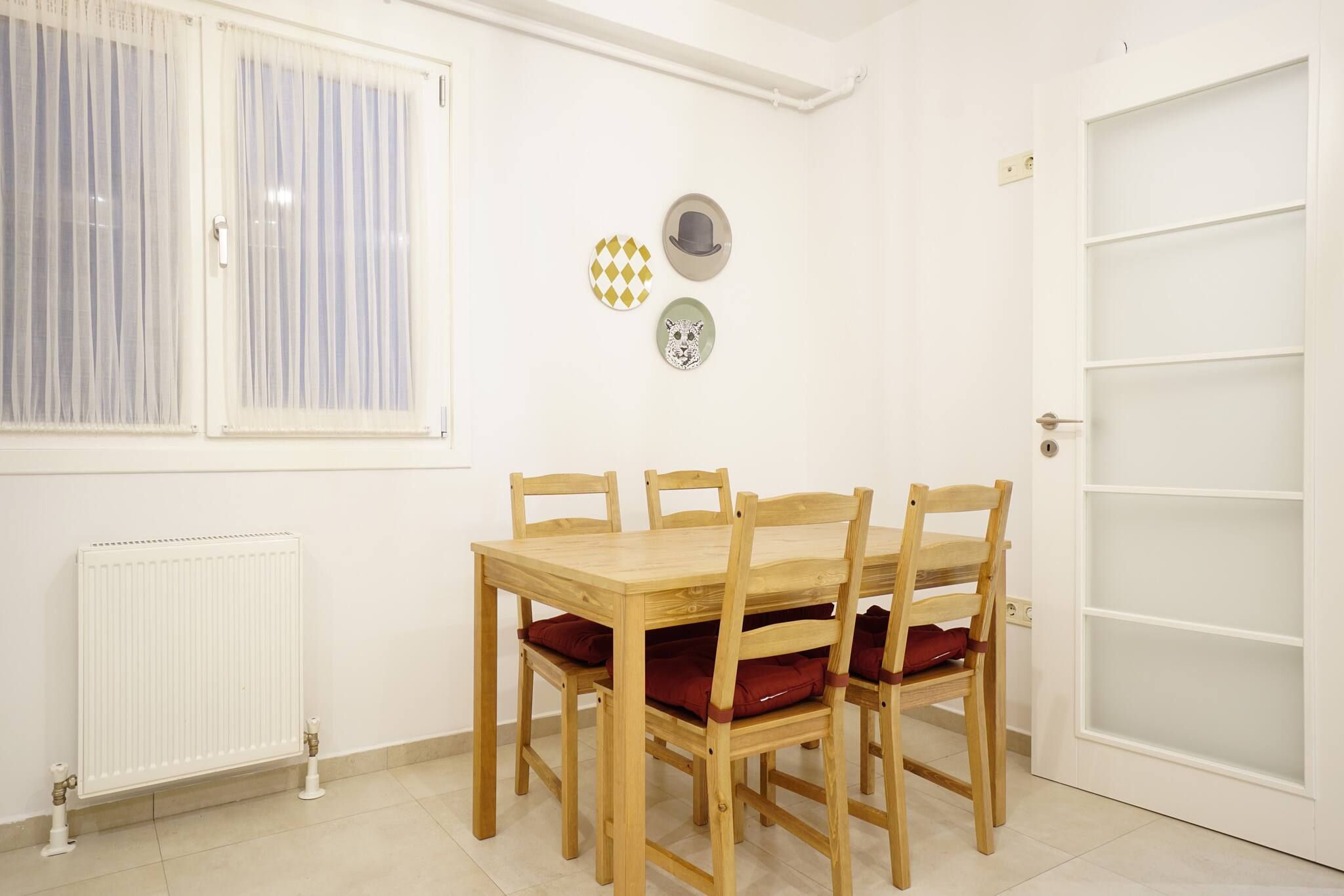 A dining area with a wooden table and chairs, a radiator, a window with curtains, and wall decorations.