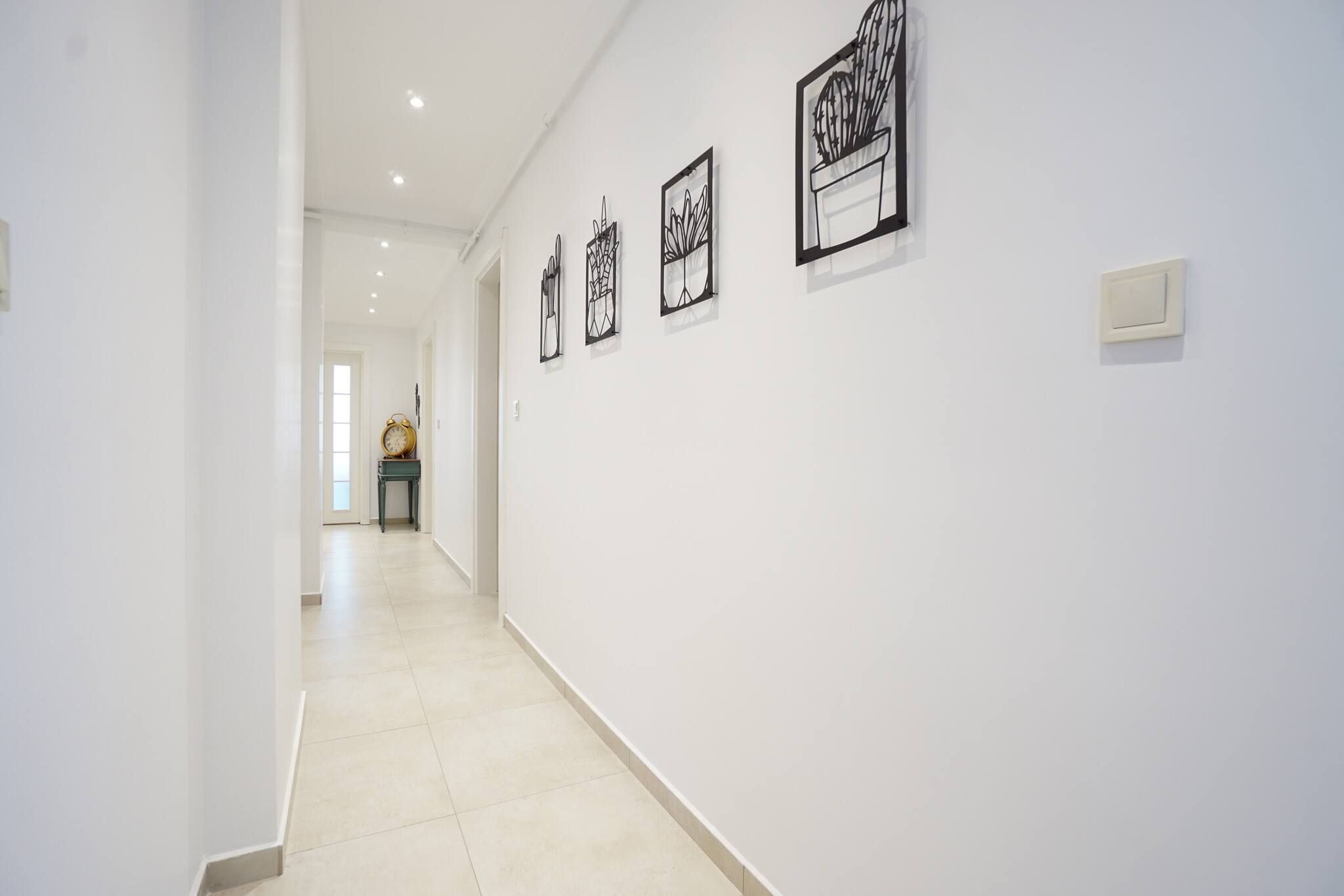 A hallway with white walls and a tiled floor, leading to a room with a door at the end.