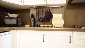 A kitchen with white cabinets, a black toaster, hanging utensils, and a wooden cutting board with a cityscape design.