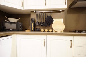A kitchen with white cabinets, a black toaster, hanging utensils, and a wooden cutting board with a cityscape design. - Elite, Tastefully Furnished, 3BR (Kadıköy)
