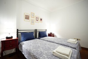 Ein Doppelbett mit gemusterten Bettbezügen, ein Nachttisch mit Lampe und eine Wand mit gerahmten Kunstwerken.