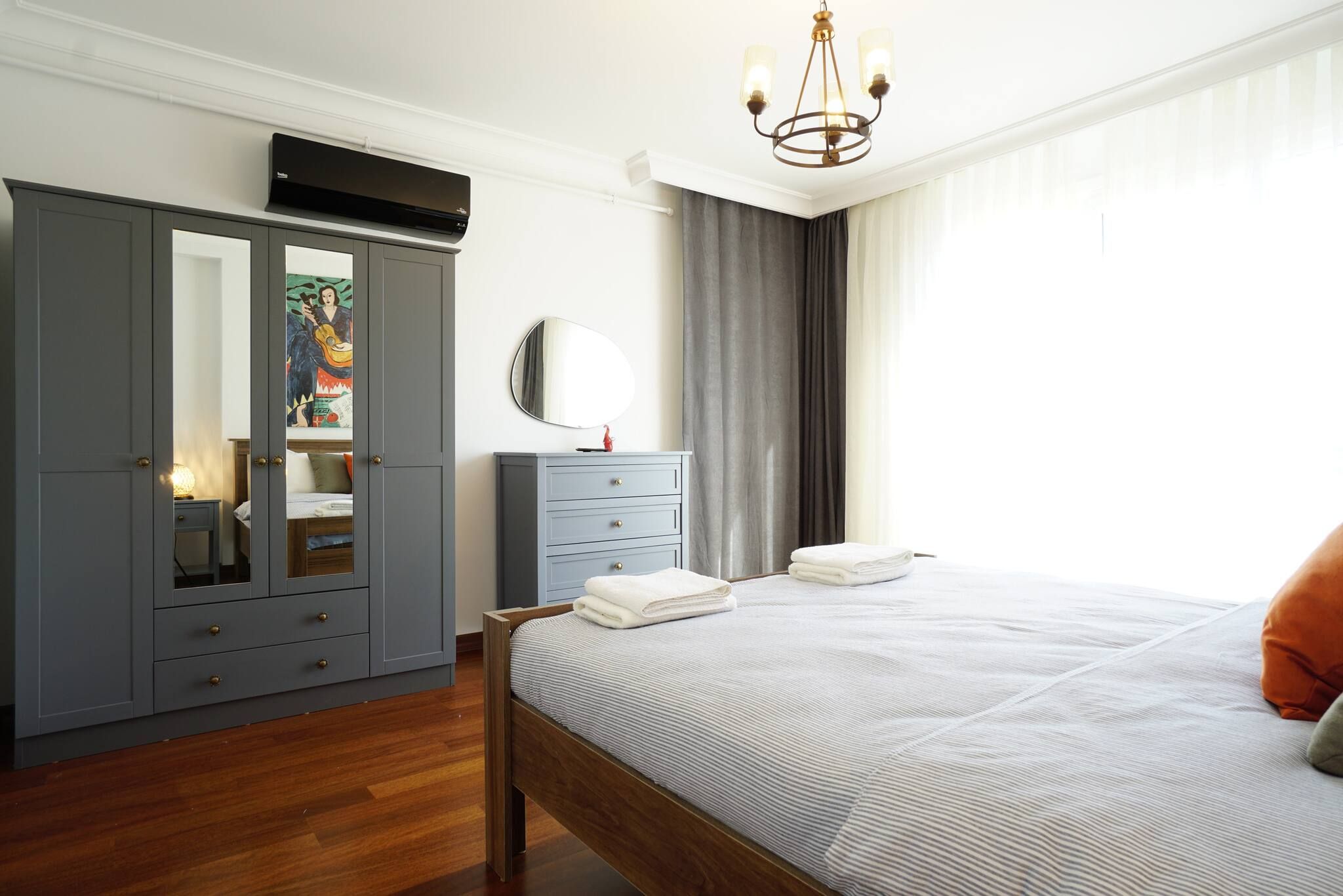 A bedroom with a bed, a wardrobe, a bedside table, a mirror, and a window with curtains.