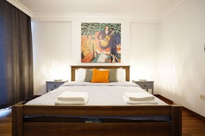 Een hotelkamer met een groot bed, twee nachtkastjes, een schilderij aan de muur en een raam met gordijnen.