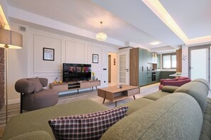 A modern living room with a flat-screen TV, a sofa set, a coffee table, and a kitchen area visible through an open door. - Polaris, Peaceful 2BR, Best Loc (Kadıköy)