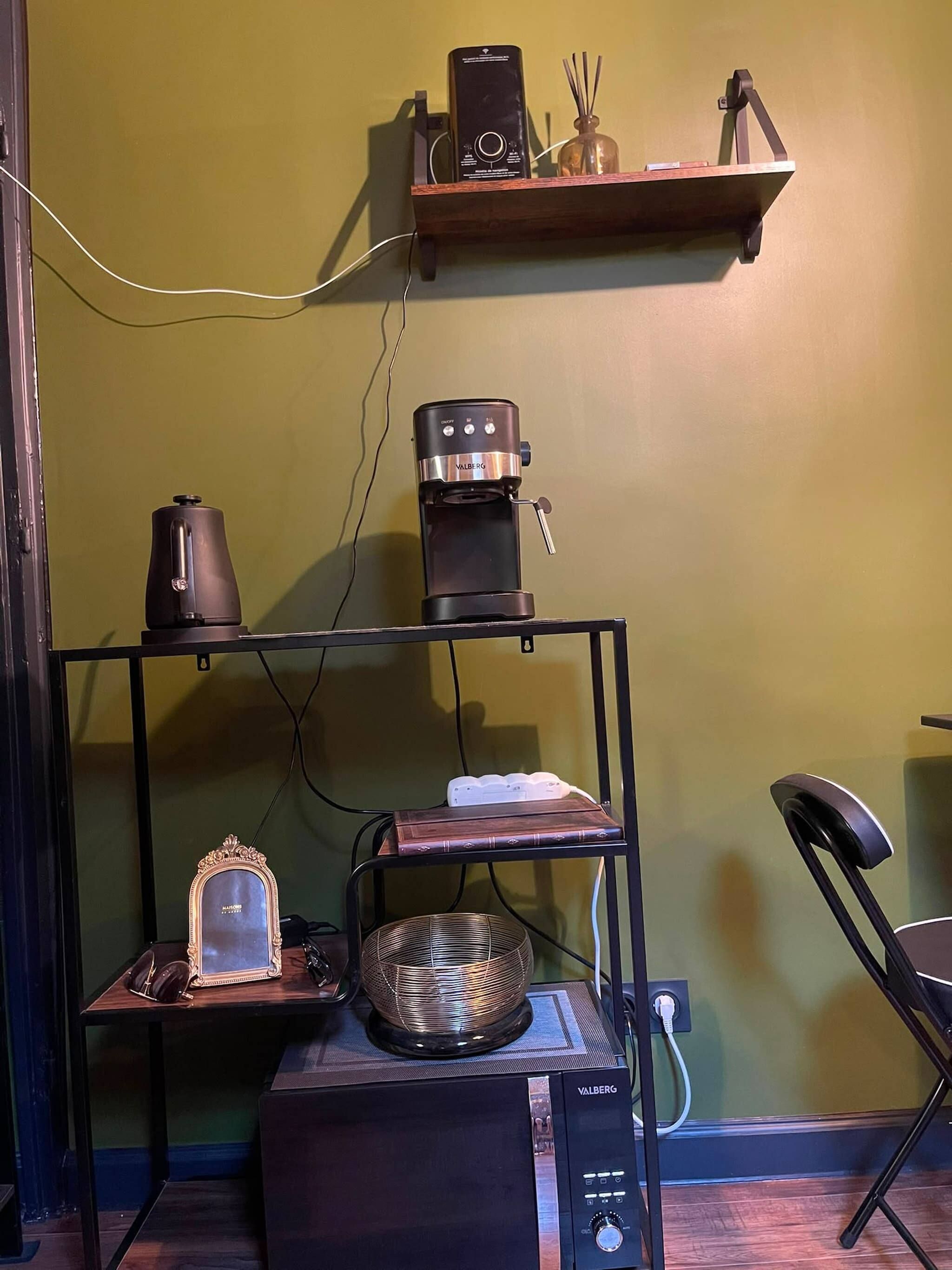 Una stanza con una macchina del caffè, uno specchio e uno scaffale con un libro e un oggetto decorativo.