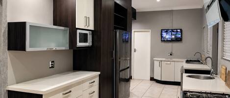 A modern kitchen with a built-in microwave, a refrigerator, a stove, and a television mounted on the wall.