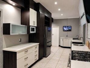 Una cocina moderna con microondas integrado, refrigerador, estufa y televisor montado en la pared.