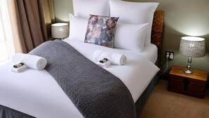 A neatly made bed with white and gray linens, a decorative pillow, and two rolled towels. - Luxurious 5-Bedroom House Rental in Springs, South Africa (Springs)