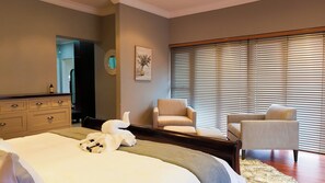 Een slaapkamer met een bed, twee stoelen, een dressoir en een raam met zonwering.