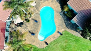 A swimming pool surrounded by a patio area with outdoor furniture and palm trees. - Luxurious 5-Bedroom House Rental in Springs, South Africa (Springs)