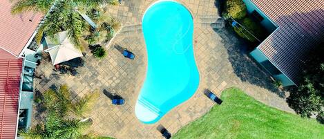 An aerial view of a swimming pool surrounded by a patio area with chairs and umbrellas.