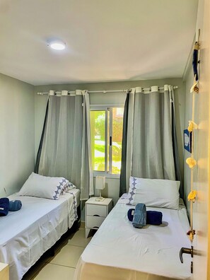 Ein Hotelzimmer mit zwei Betten, einem Fenster mit Vorhängen, einem Nachttisch mit Lampe und einer Tür mit Griff.