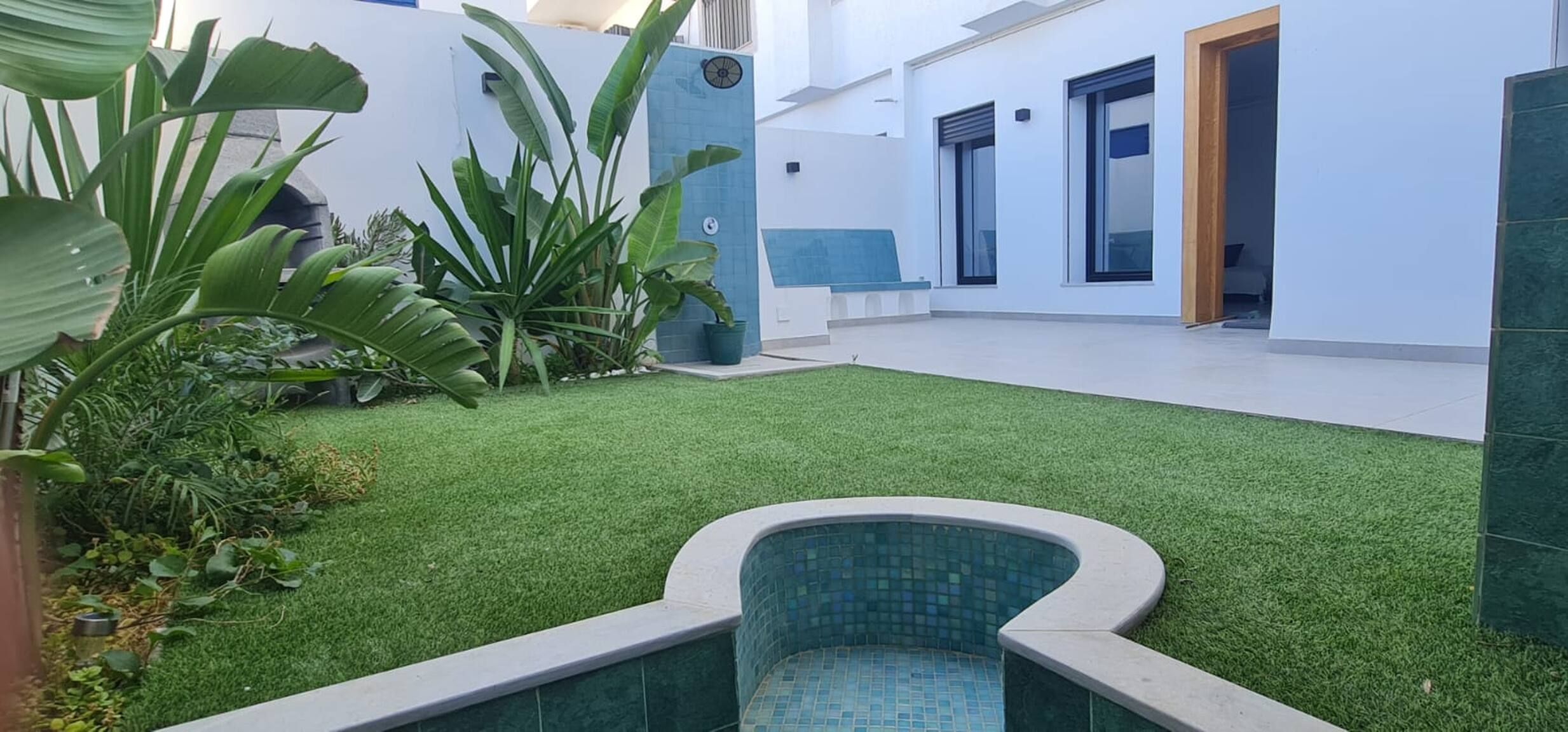 Un espace extérieur moderne avec une pelouse artificielle, une petite piscine et des plantes en pot.