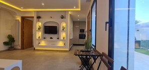 Un intérieur moderne avec un téléviseur central, un éclairage encastré et un coin repas doté d’une banquette.
