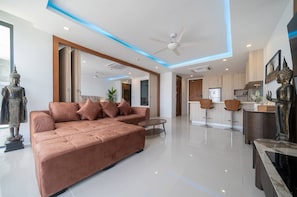 A modern living room with a sofa, a dining area with bar stools, and a kitchen. - Apartment with Sea View and Hot Tub on Balcony (Rawai)