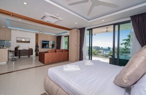 A modern hotel room with a large bed, a sofa, a dining area, and a balcony with a view. - Apartment with Sea View and Hot Tub on Balcony (Rawai)
