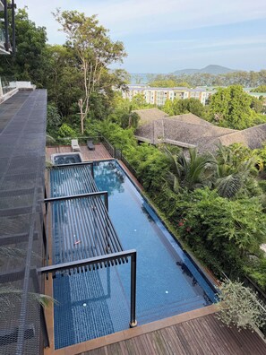 A rooftop infinity pool with a wooden deck, surrounded by lush greenery and overlooking a residential area. - Apartment with Sea View and Hot Tub on Balcony (Rawai)