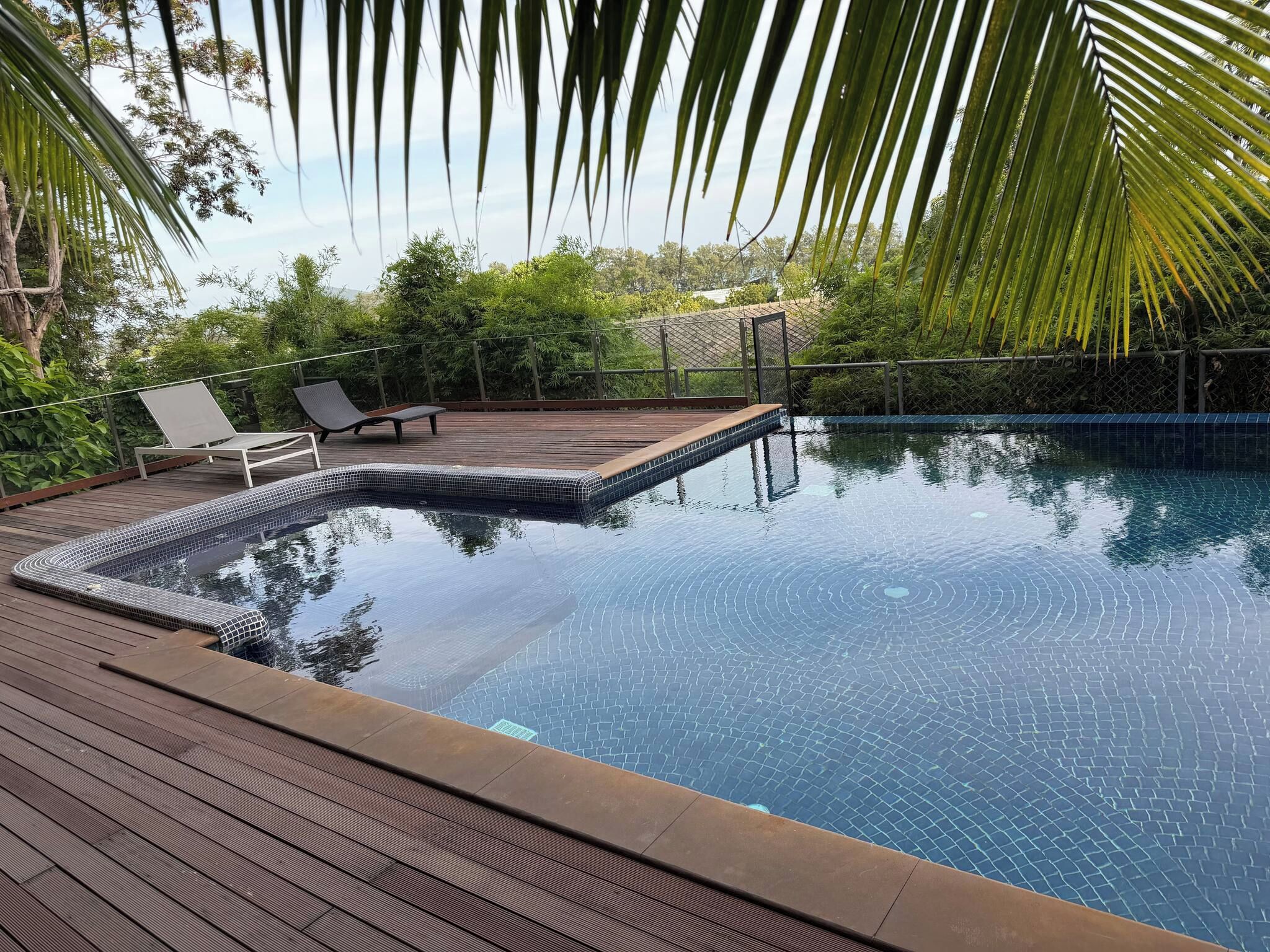 A clear swimming pool with a wooden deck and lounge chairs.