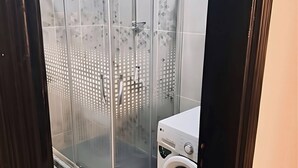 Ein modernes Badezimmer mit Duschkabine aus Glas, einer Waschmaschine und Fliesenboden.