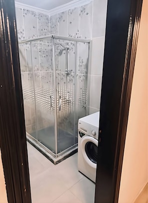 Um banheiro moderno com box de vidro, máquina de lavar e piso revestido.