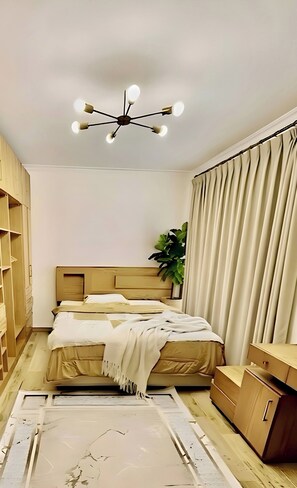 Quarto com cama, luminária no teto, planta e guarda-roupa.