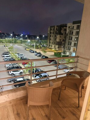 Varanda com cadeiras de vime, com vista para um estacionamento com vários carros e um edifício alto ao fundo.