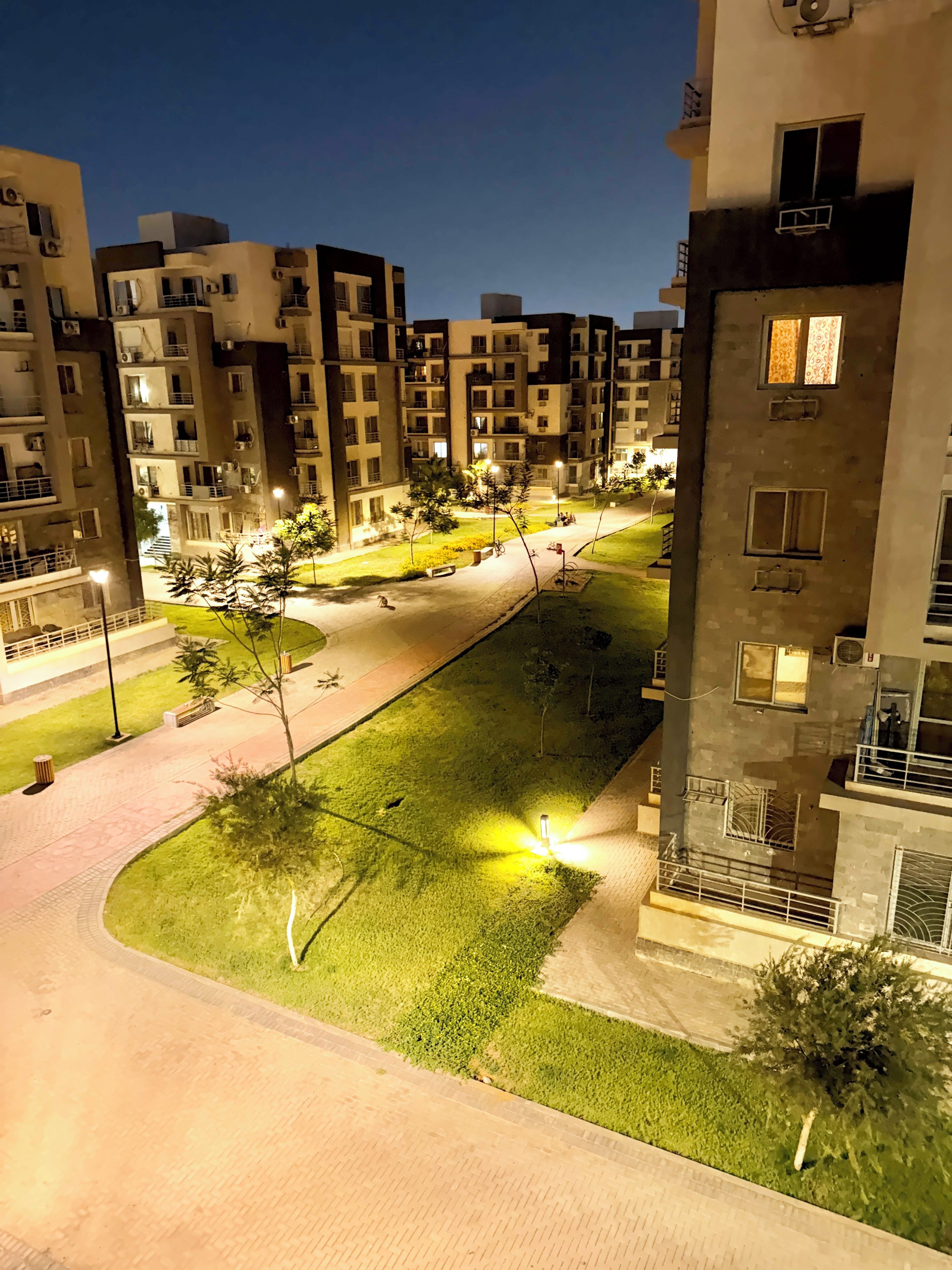 A residential building complex at night with illuminated pathways and greenery.