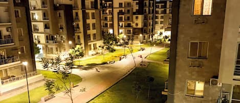 Un ensemble d’immeubles résidentiels la nuit, avec des allées éclairées et de la végétation.