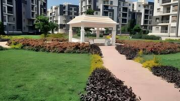 A modern residential complex with a central garden area featuring a gazebo, a paved walkway, and well-maintained greenery.