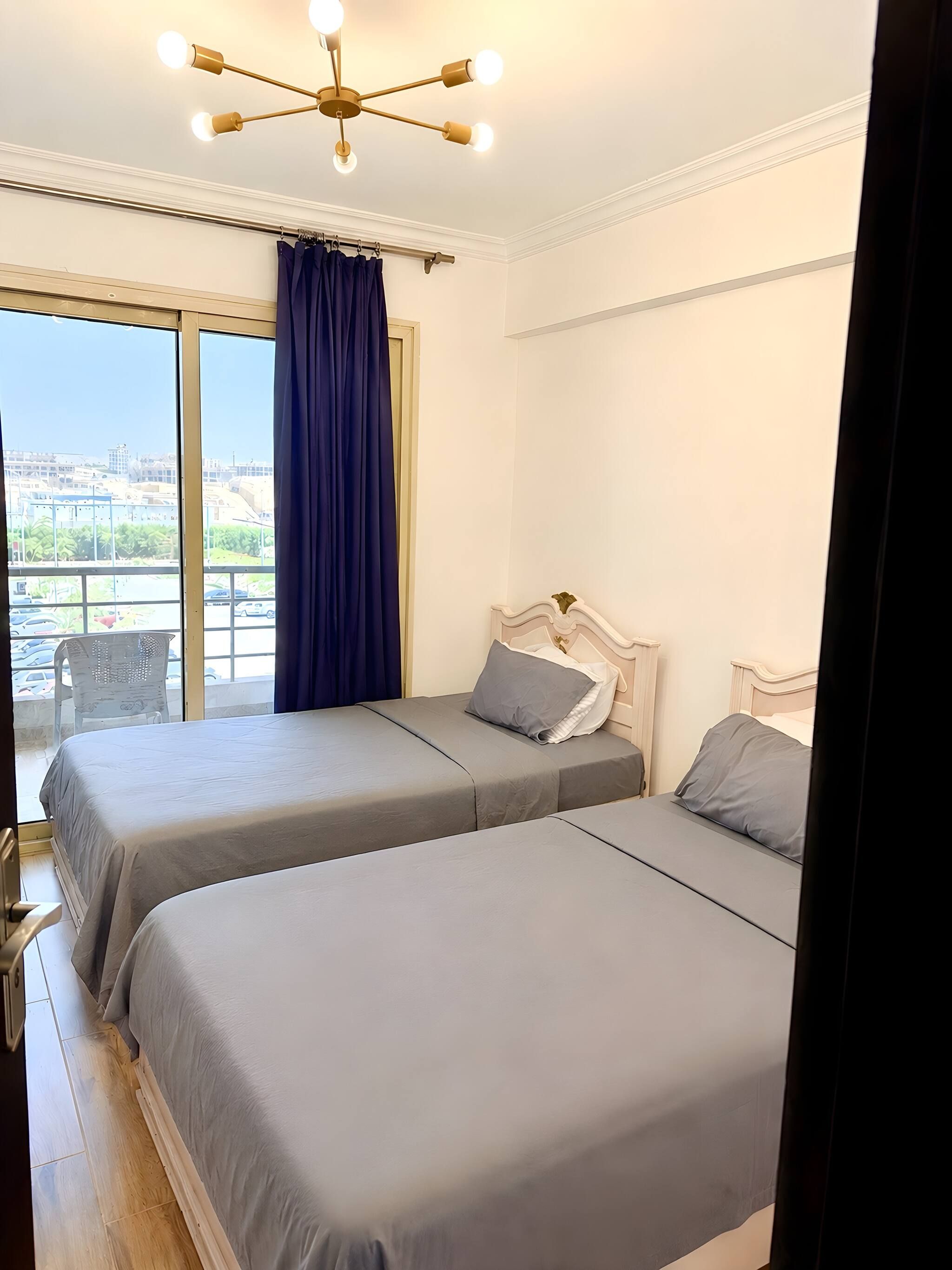 A hotel room with two beds, a large window with curtains, and a ceiling light fixture.