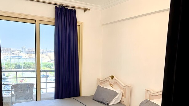 Ein Hotelzimmer mit zwei Betten, einem großen Fenster inklusive Vorhängen und einer Deckenleuchte.