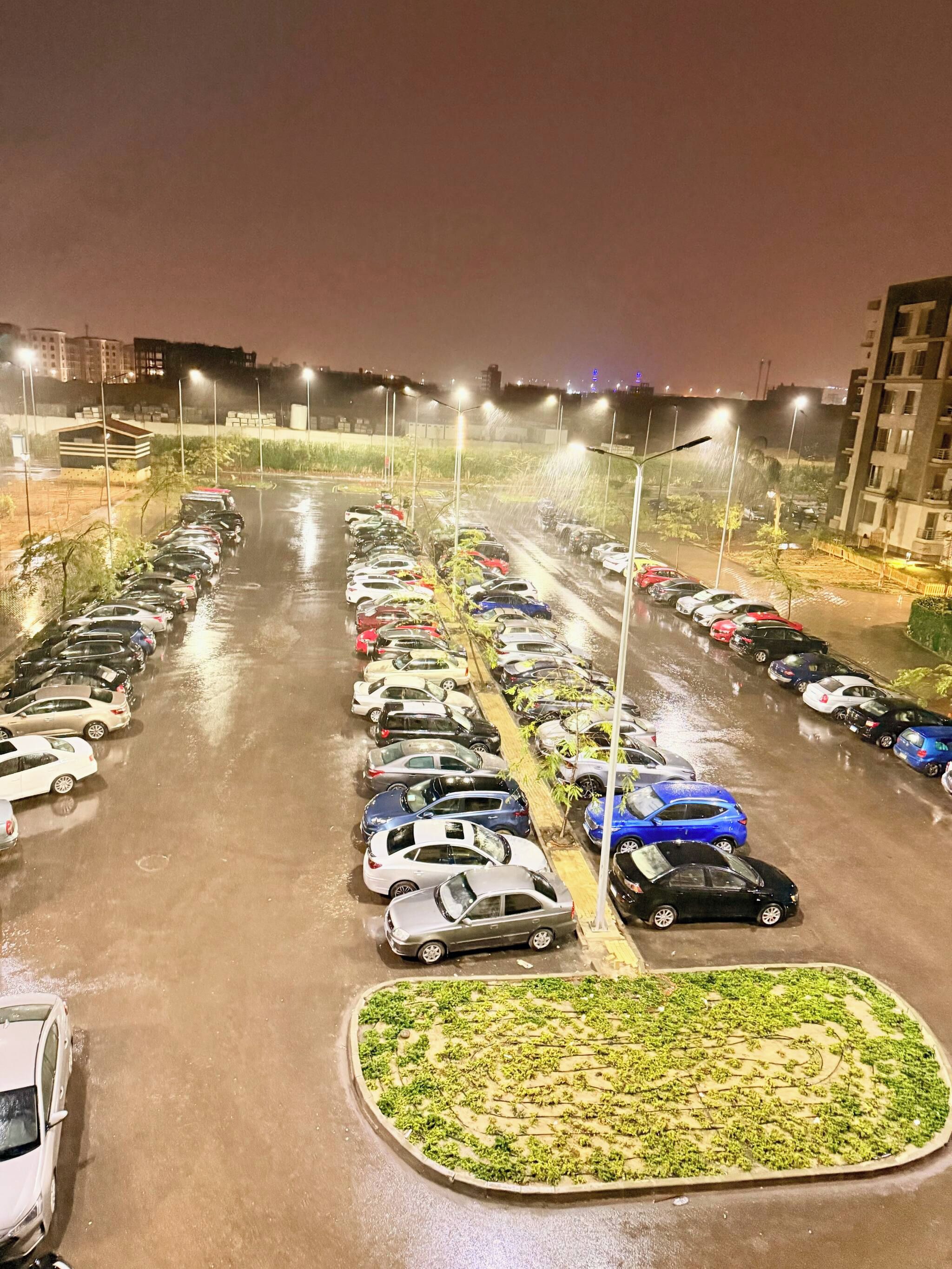 Estacionamento com várias fileiras de carros estacionados e um espaço central com paisagismo.
