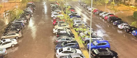 Un estacionamiento con varias filas de automóviles estacionados, iluminado por luces colgantes.