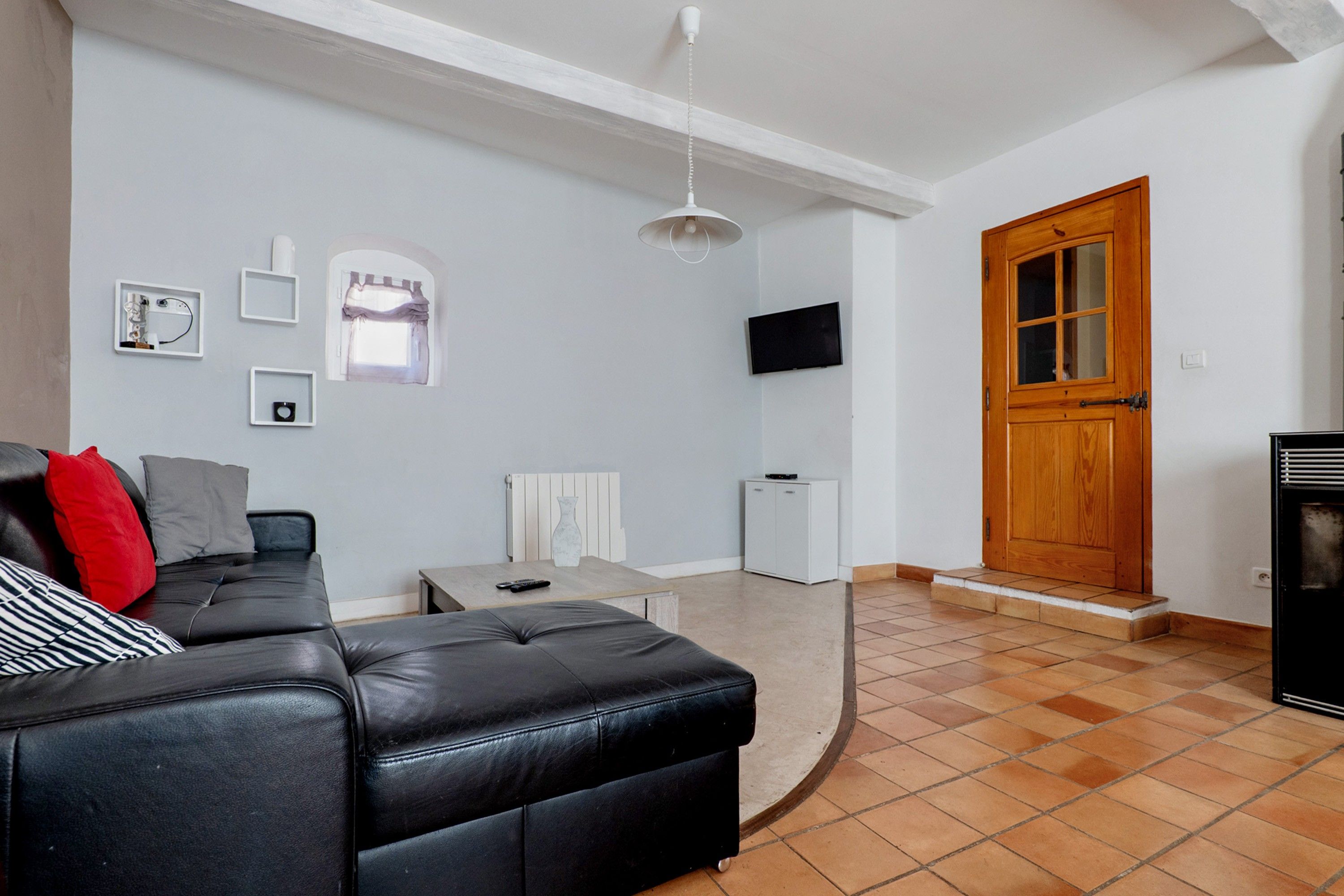Una sala de estar con un sofá de cuero negro, un radiador blanco, un televisor y una puerta de madera.