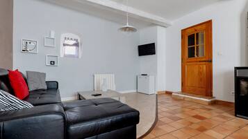 Una sala de estar con un sofá de cuero negro, un radiador blanco, un televisor y una puerta de madera.